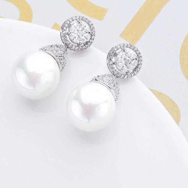 Drop pearl earrings with diamond-like stones on a white background