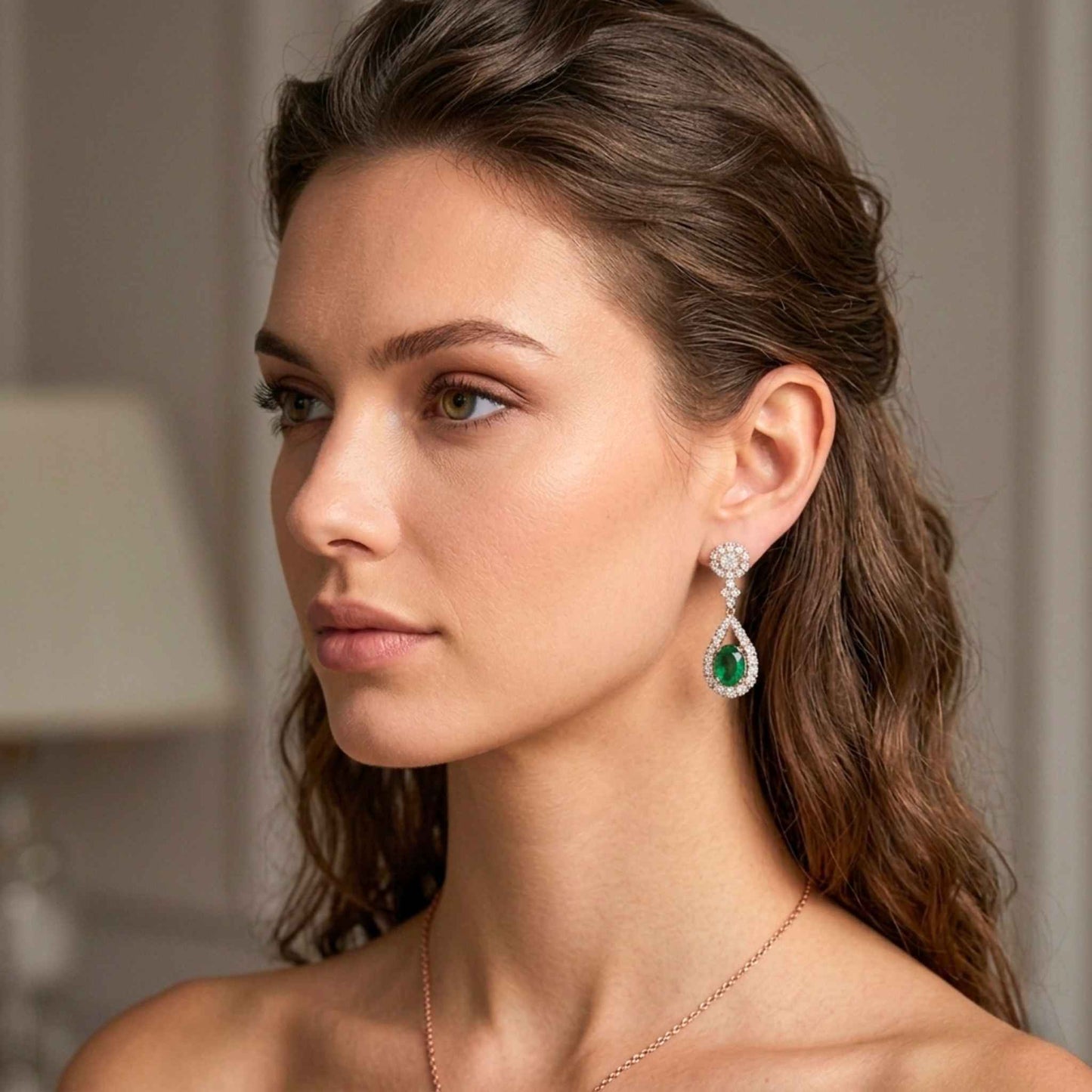 Close-up of rose gold plated teardrop earring with oval green cubic zirconia surrounded by sparkling white stones against a blurred background. Digitally rendered model for scale.