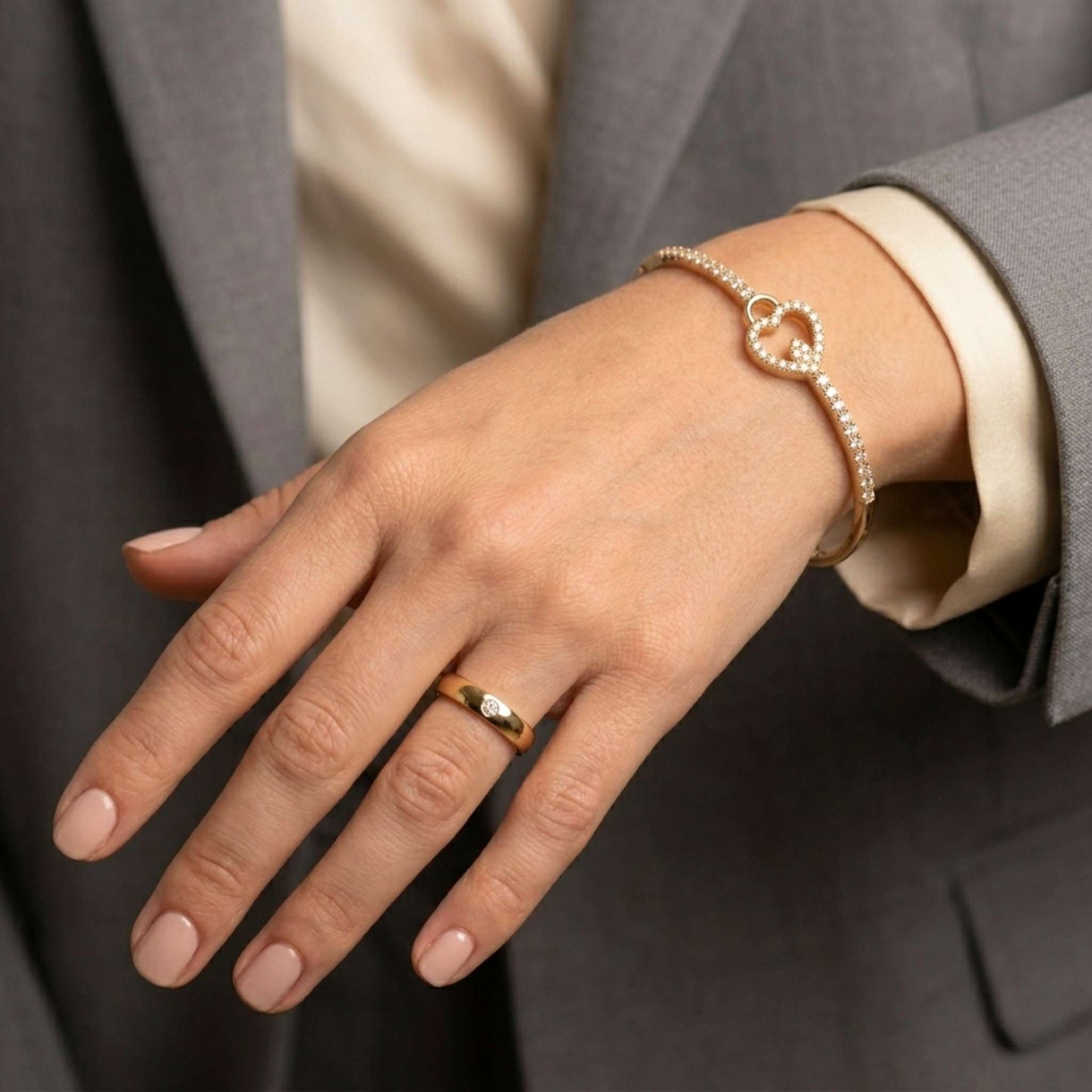 Close up of a women wearing a grey brown jacket of her hand with a gold ring and bracelet with heart design and sparkling gemstones.  Digitally rendered model for scale