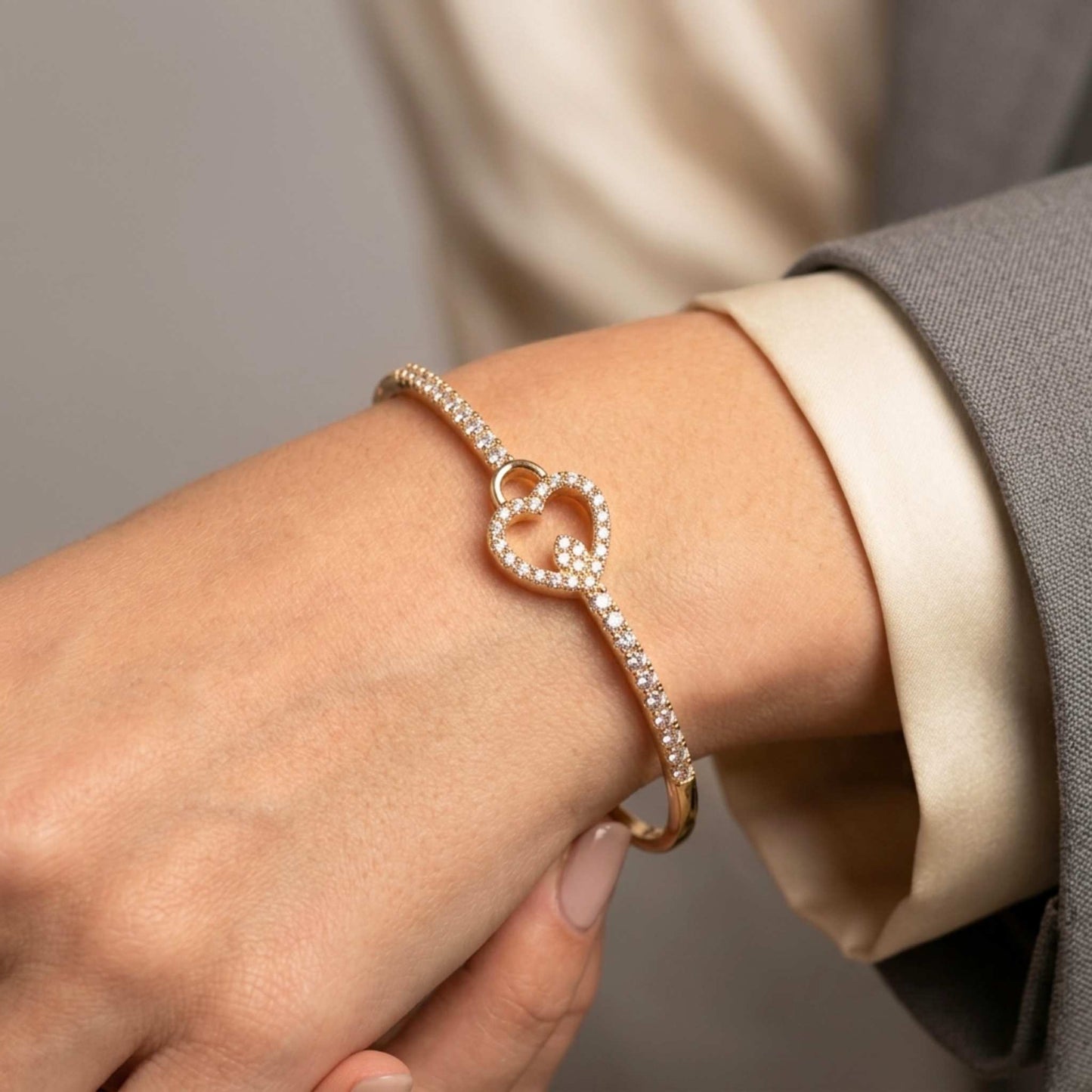 Close-up of a hand wearing a gold bangle bracelet with a heart design and adorned with gemstones. Digitally rendered model for scale