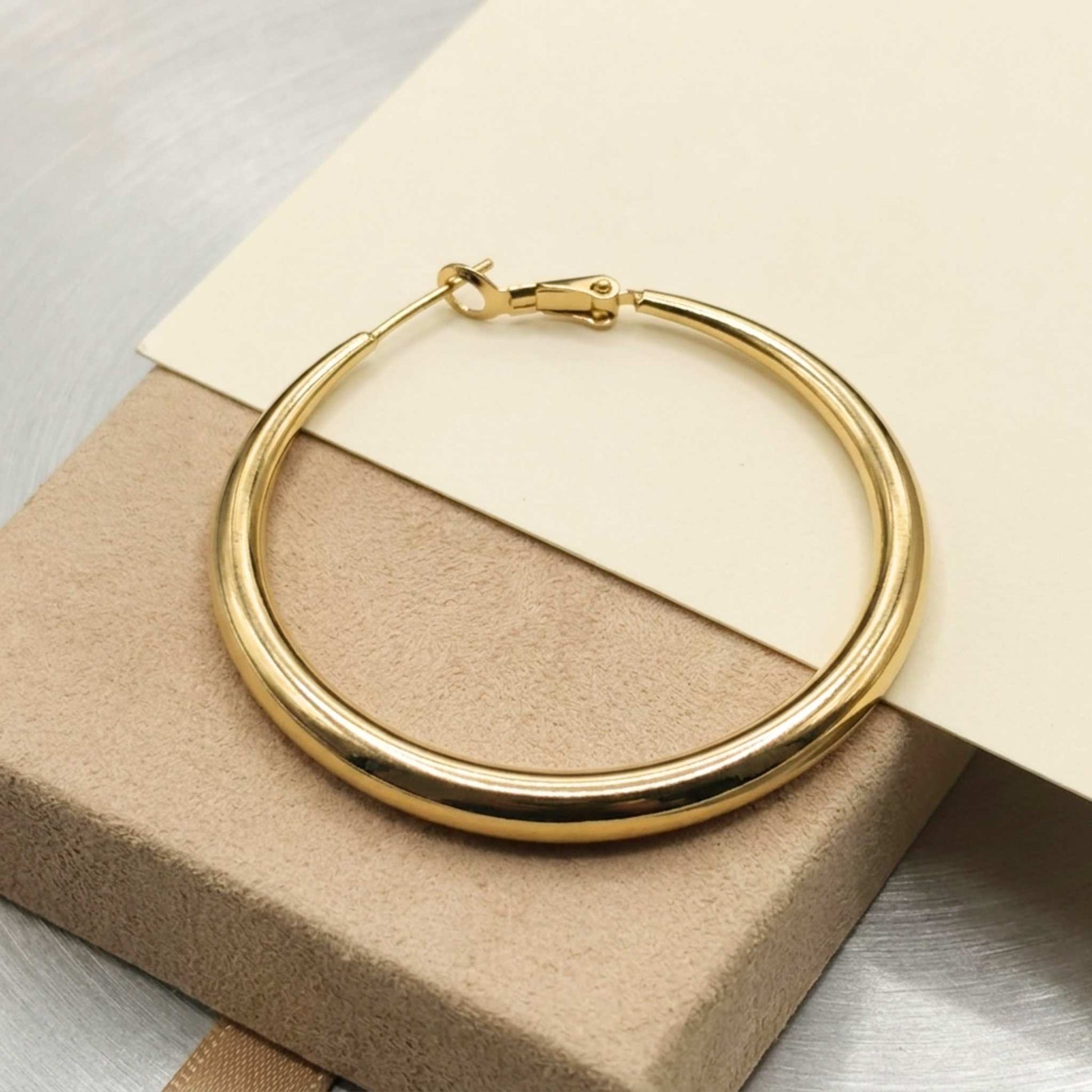 Gold hoop earring on a beige box with a neutral background