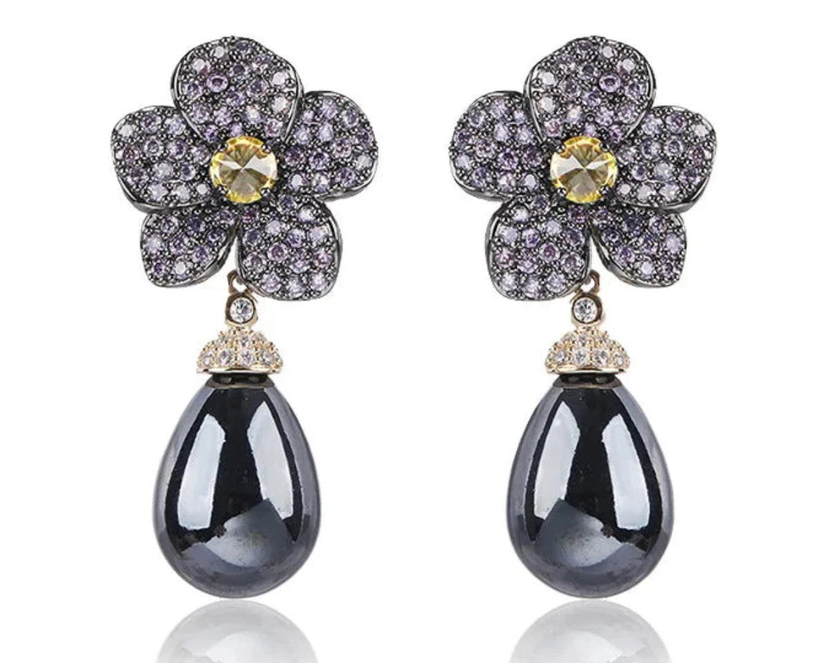 Pearl drop earrings with a main dark grey gemstone hung from a beautiful floral arrangement of delicate pinks and yellow gemstone against a white background. 