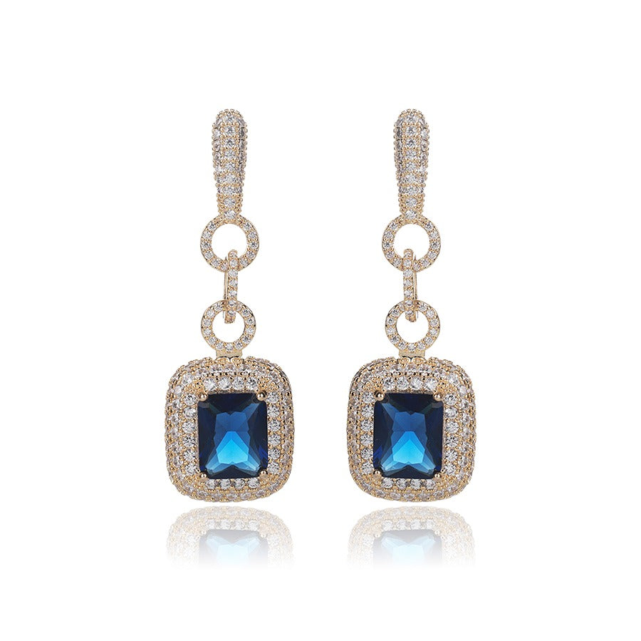 Pair of elegant drop earrings with blue zirconia stones and gold accents on a white background.