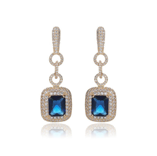 Pair of elegant drop earrings with blue zirconia stones and gold accents on a white background.