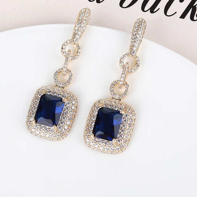 Pair of blue earrings adorned with sparkling zirconia stones and gold accents on a white surface.