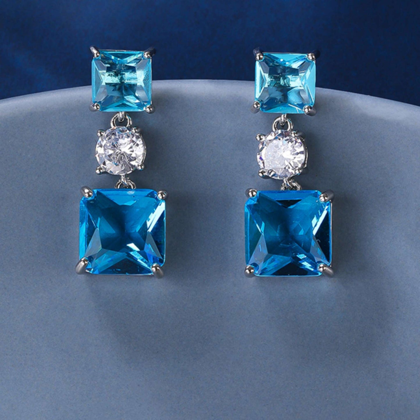 Plain of blue square earrings set against a plain blue background.