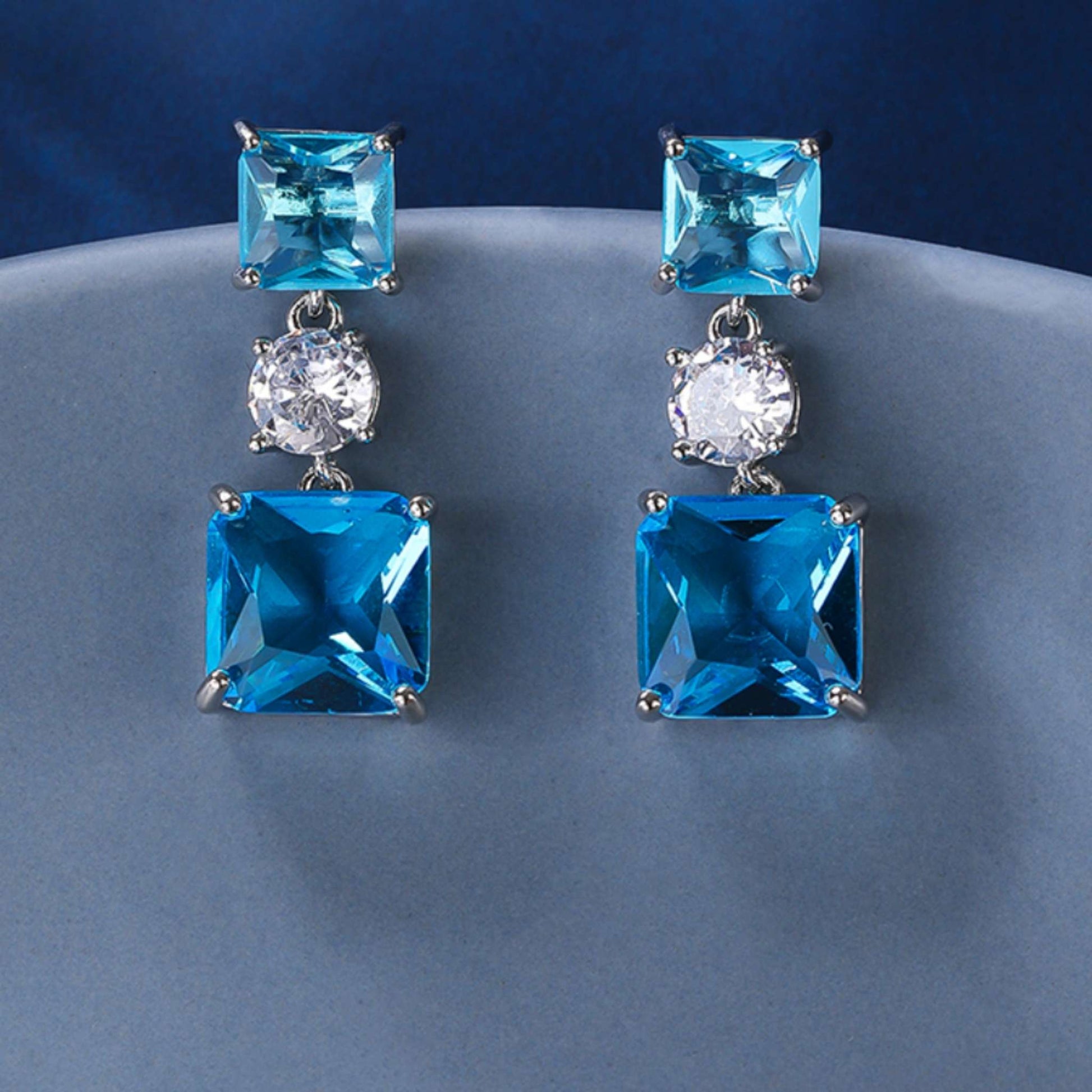 Plain of blue square earrings set against a plain blue background.