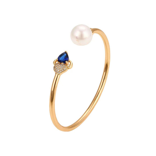 Gold bracelet with a pearl and sapphire blue gemstone in a bangle design on a white background