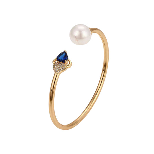 Gold bracelet featuring a pearl and sapphire blue gemstone in a bangle design against a white background