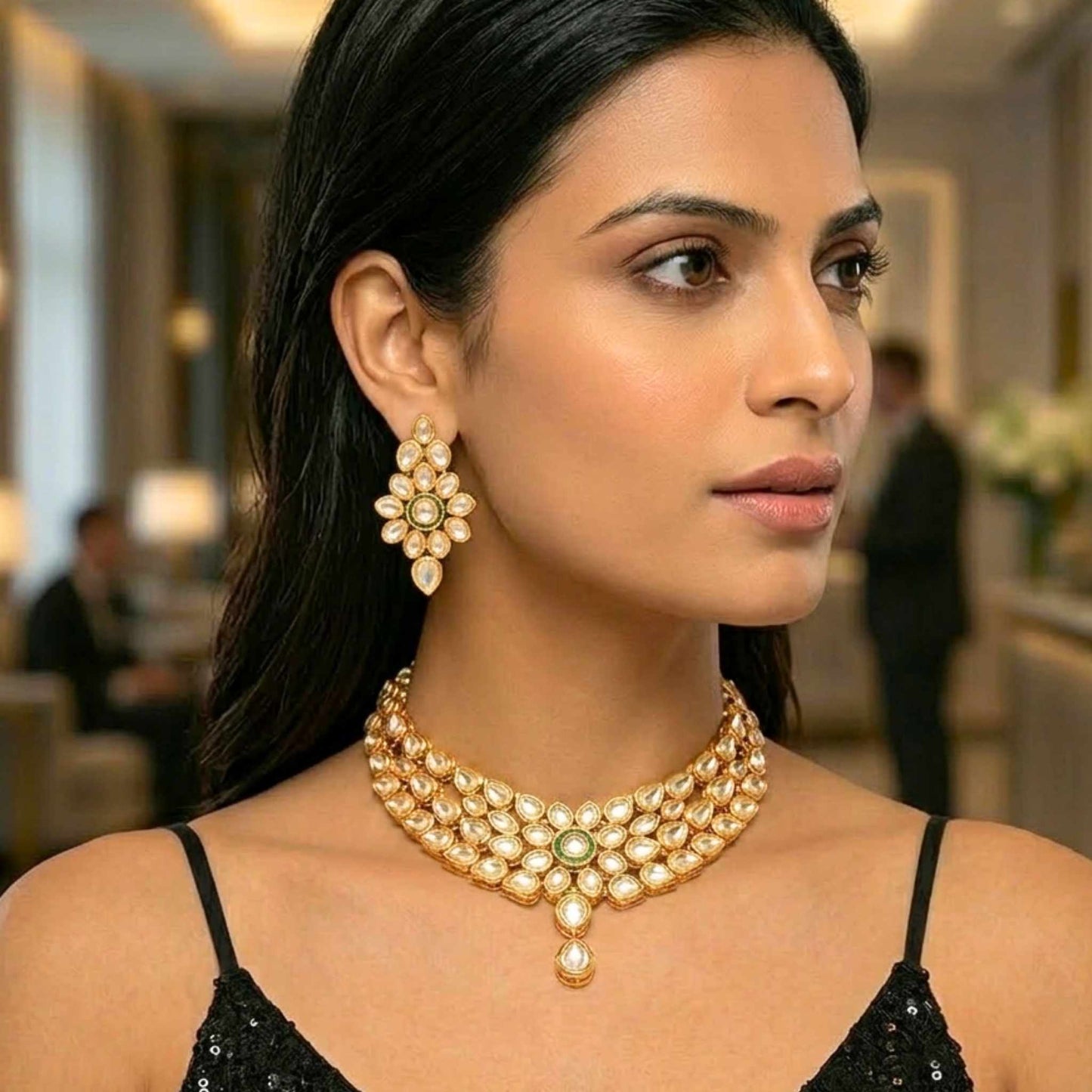 Woman wearing a gold choker necklace and matching earrings with a blurred formal indoor background