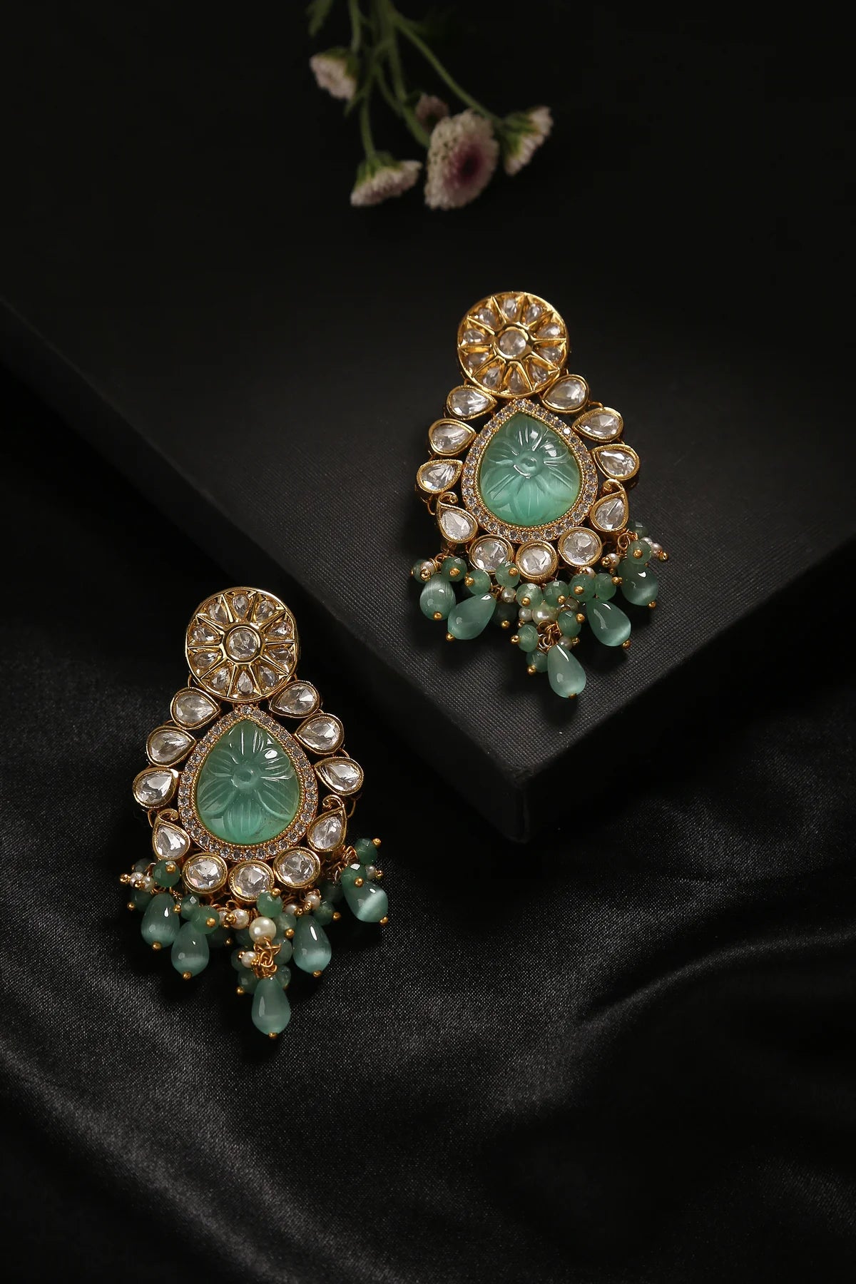 gold Indian wedding style earrings presented in beautiful pastel and dark green colours.