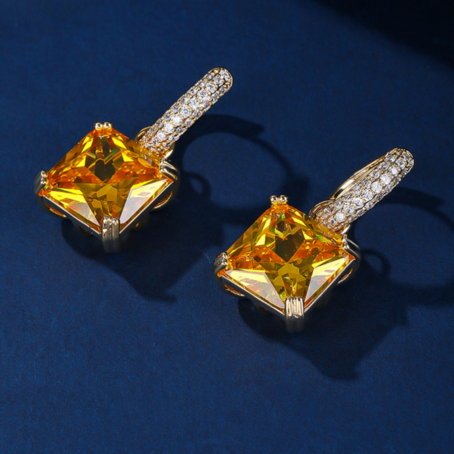 Pair of yellow drop earrings suspended from hoops against a blue background