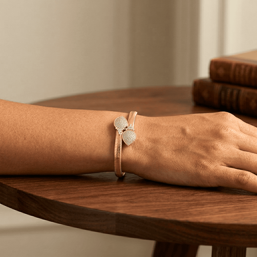 Hand wearing a rose gold bracelet on a wooden surface with a neutral background