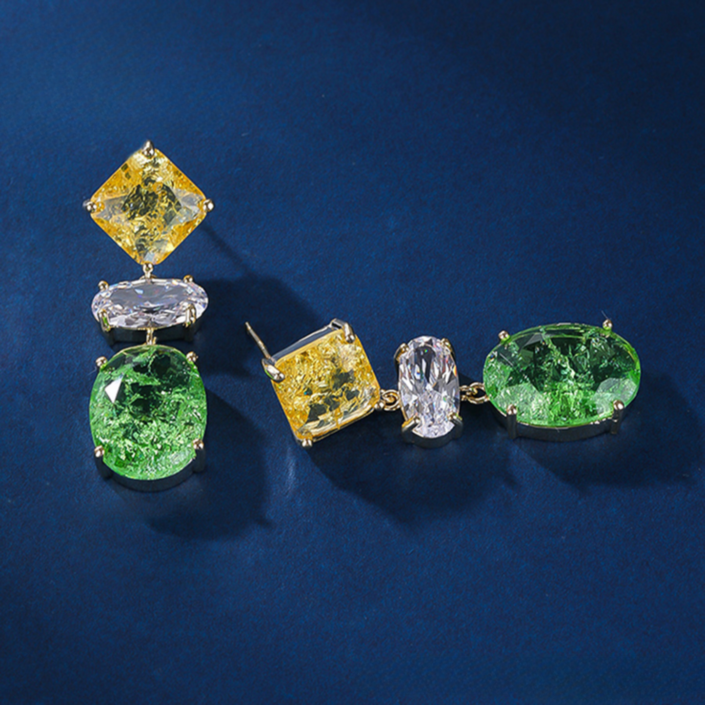 Pair of gold earrings with green and yellow gemstones on a blue background