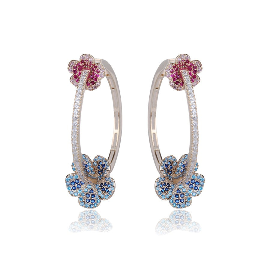 Pair of hoop earrings with floral designs featuring red and blue gemstones on a white background.