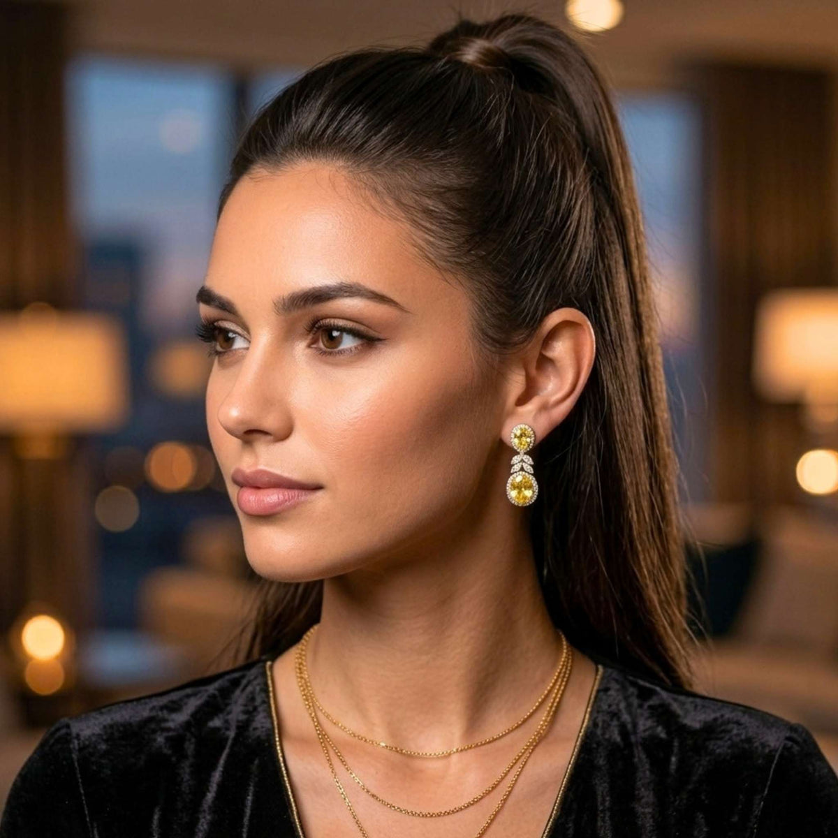 A woman with dark hair in a high ponytail is shown in profile, wearing a pair of gold and white drop topaz earrings from the Jewellery 4 Elegance collection, layered gold necklaces, and a black velvet top against a softly blurred indoor background.  Digitally rendered model for scale