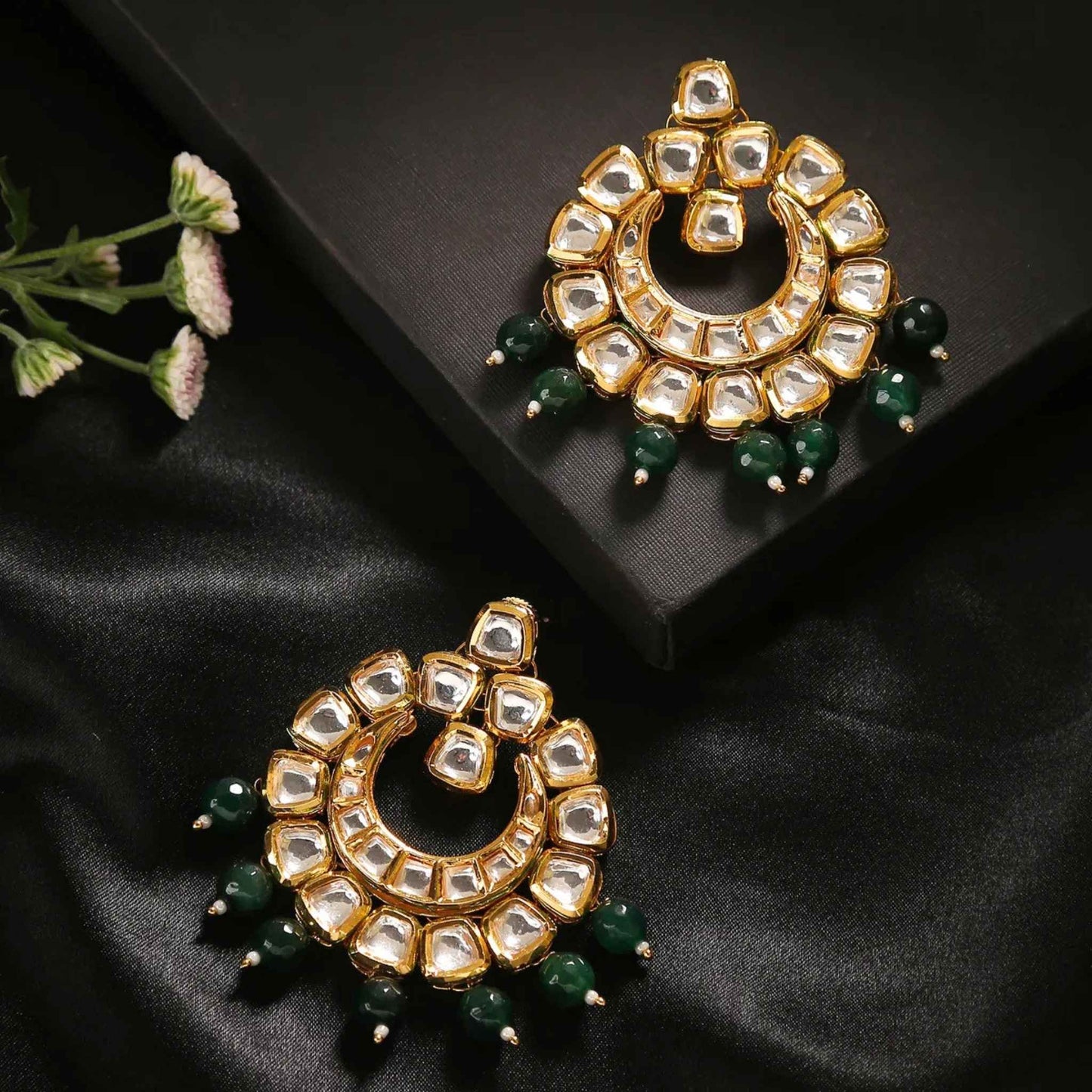 Pair of Kundan gold earrings with clear gemstones and green bead drops against a back setting.