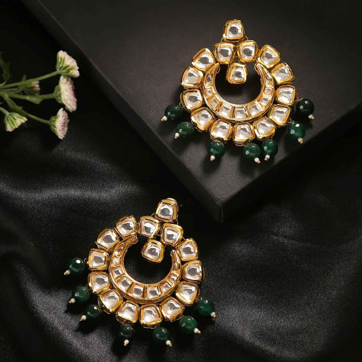 Pair of Kundan gold earrings with clear gemstones and green bead drops against a back setting.