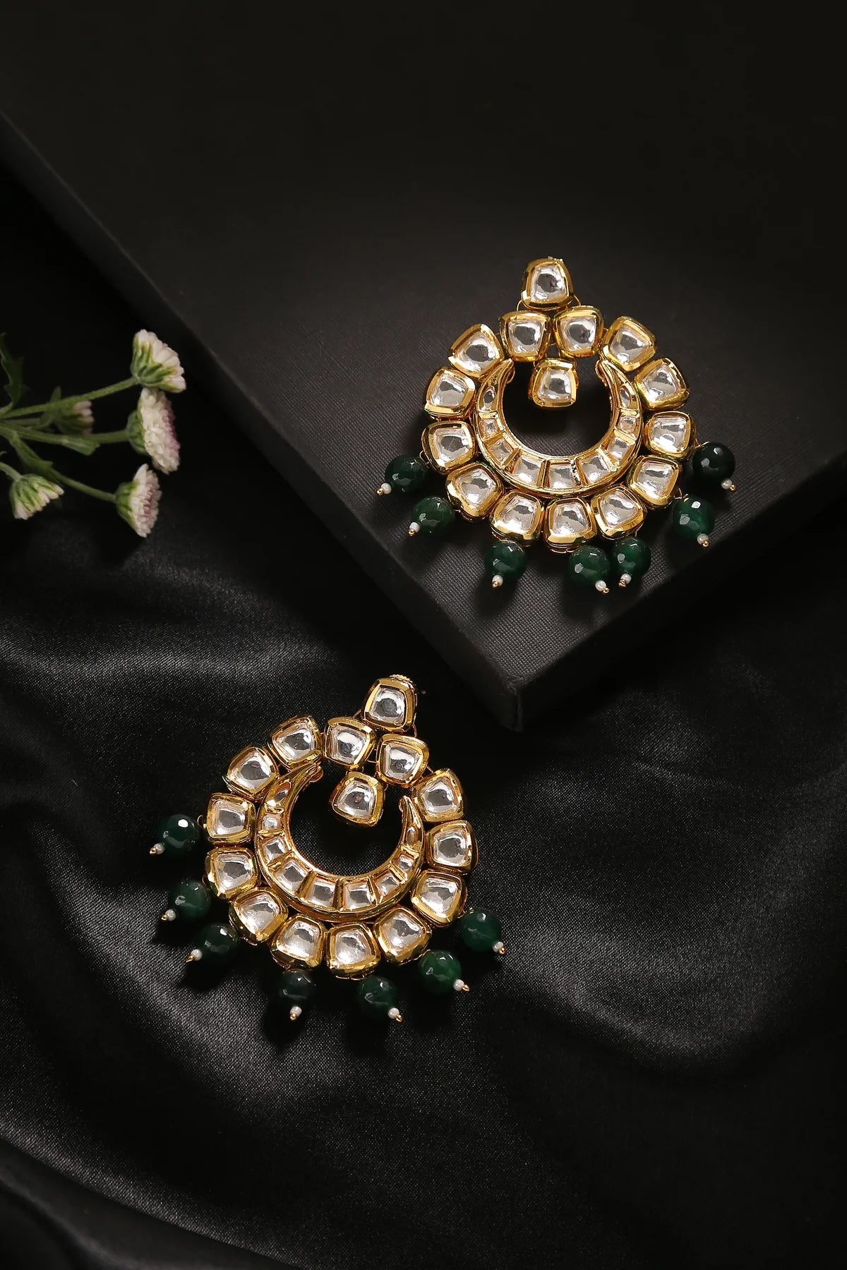 Pair of Kundan gold earrings with clear gemstones and green bead drops against a back setting.