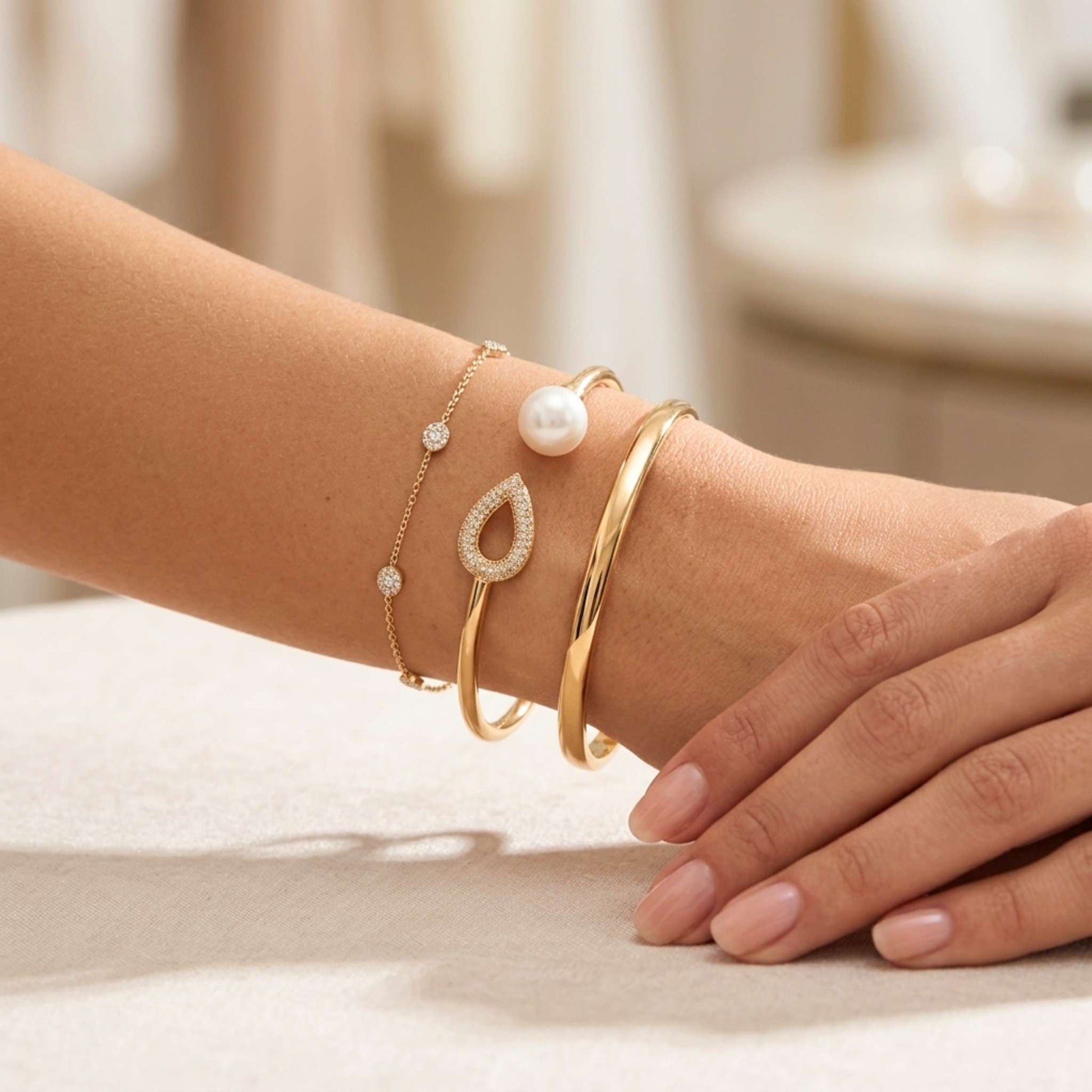 Close-up of a wrist wearing gold bracelets with pearls on a neutral background.  Digitally rendered model for scale