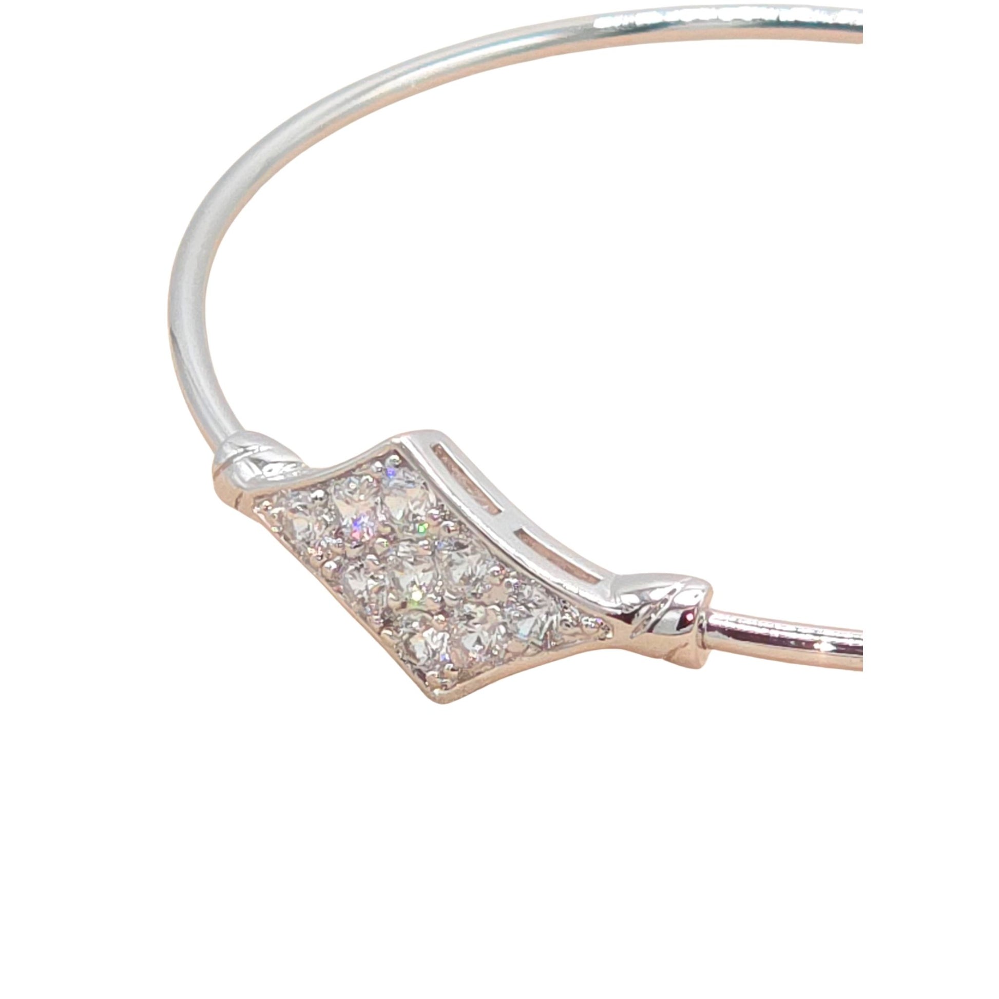 Close up of a white gold bangle bracelet with embedded gemstones on a white background.
