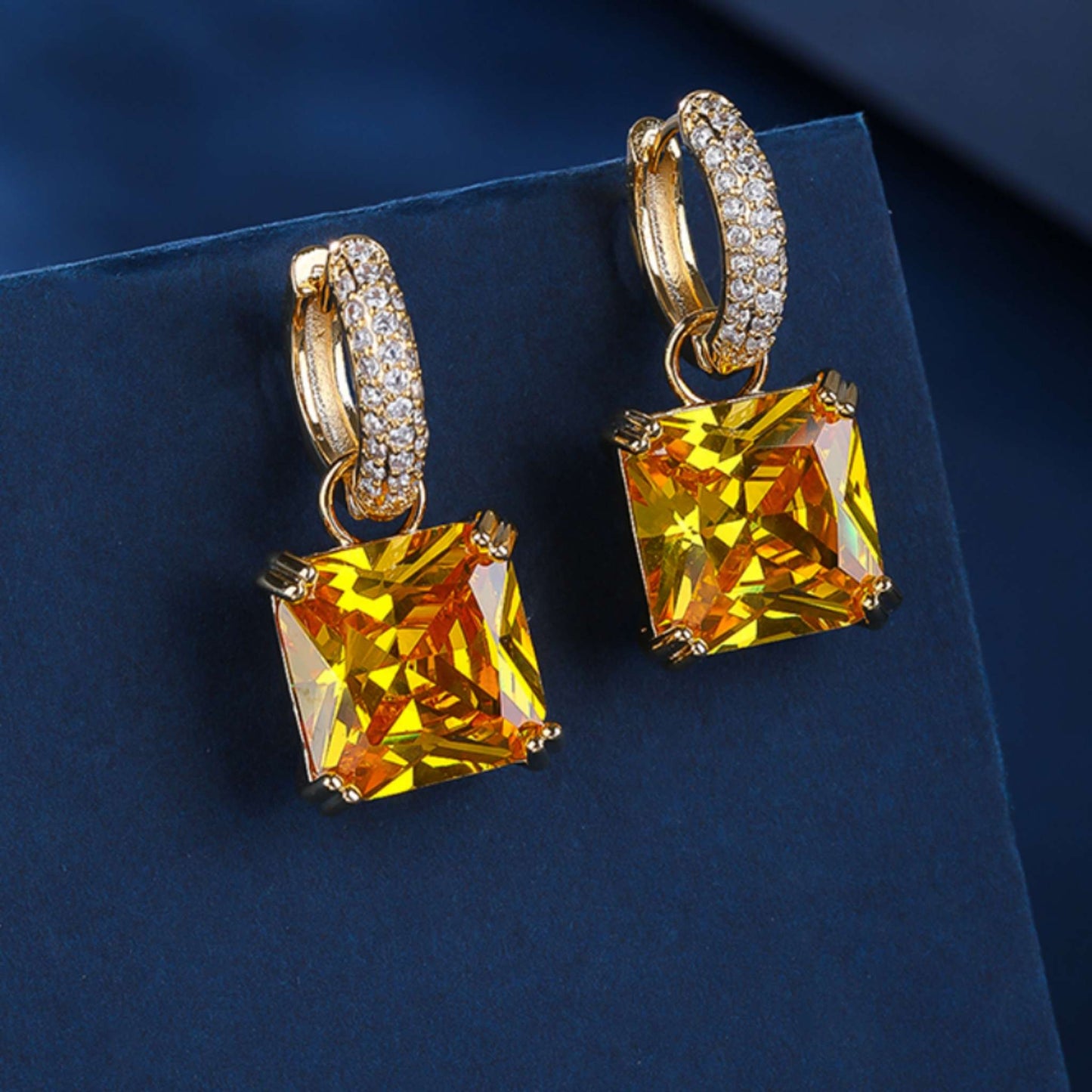Gold hoop earrings with large yellow gemstones on a dark blue background