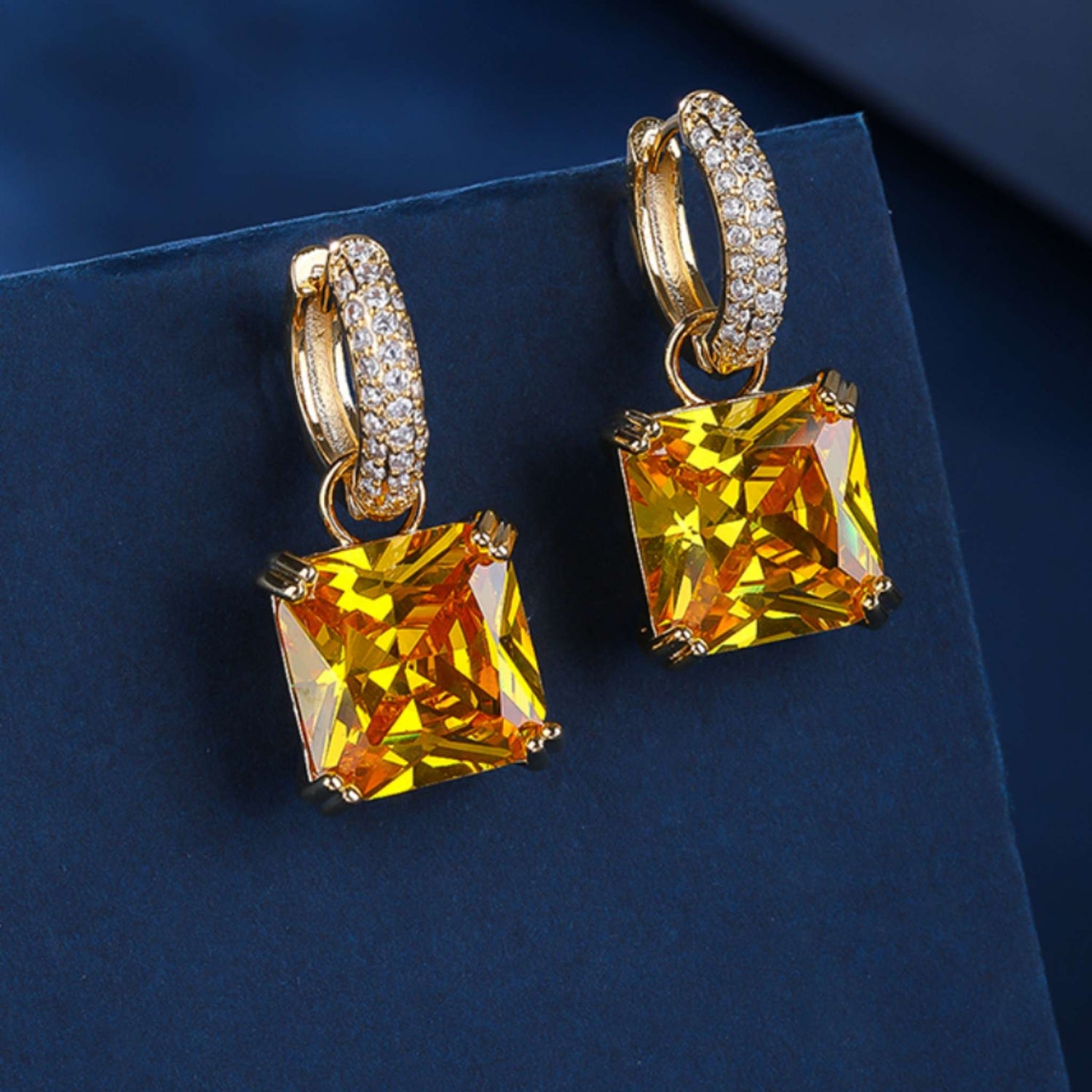 Gold hoop earrings with large yellow gemstones on a dark blue background