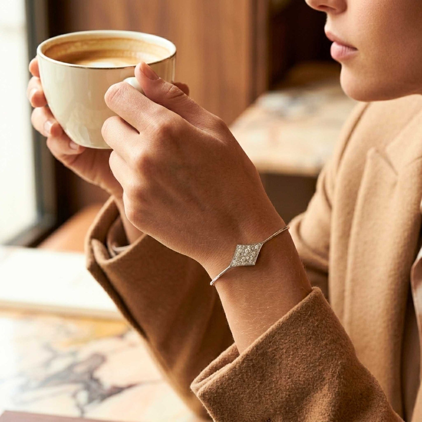 Women in brown jacket drinking coffee and wearing a white gold bracelet with sparkling gemstones from the Jewellery 4 Elegance collection.  Digitally rendered model for scale