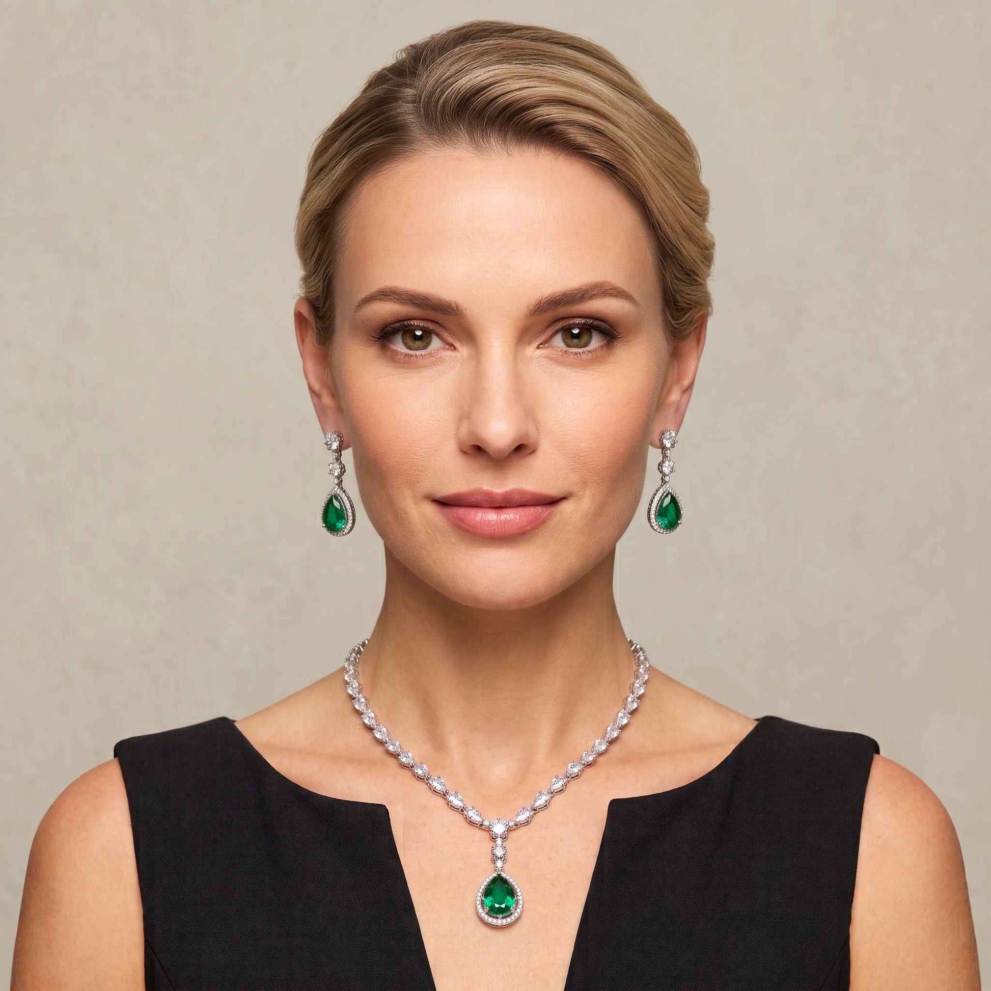 A woman with blonde hair styled in an updo wears a matching emerald green and gemstone necklace and drop earrings against a neutral beige background.  Digitally rendered model for scale.