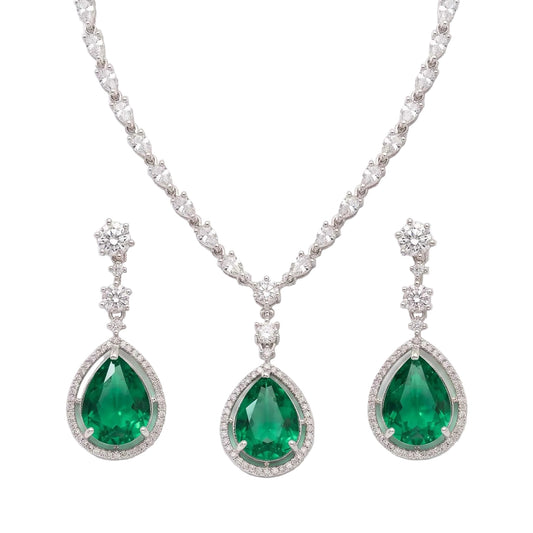 A luxury jewellery set featuring a silver-tone necklace and matching drop earrings with large pear-cut emerald green gemstones surrounded by clear pavé stones, set against a clean white background.  From the Jewellery 4 Elegance collection.