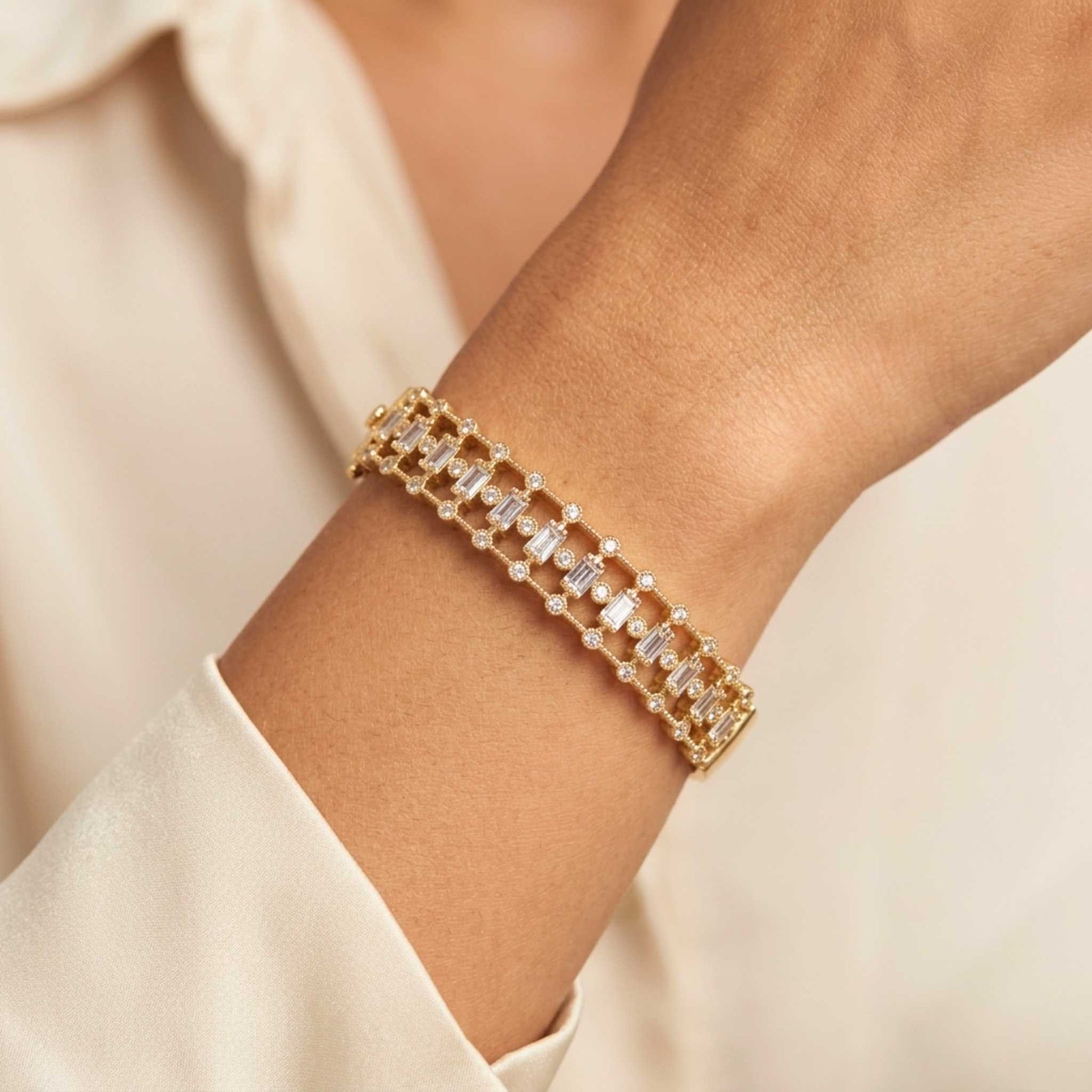 Women's wrist with a Gold-toned hinged bangle bracelet featuring an intricate front band set with vertical baguette-cut and round brilliant-cut cubic zirconia gemstones.  Digitally rendered model for scale