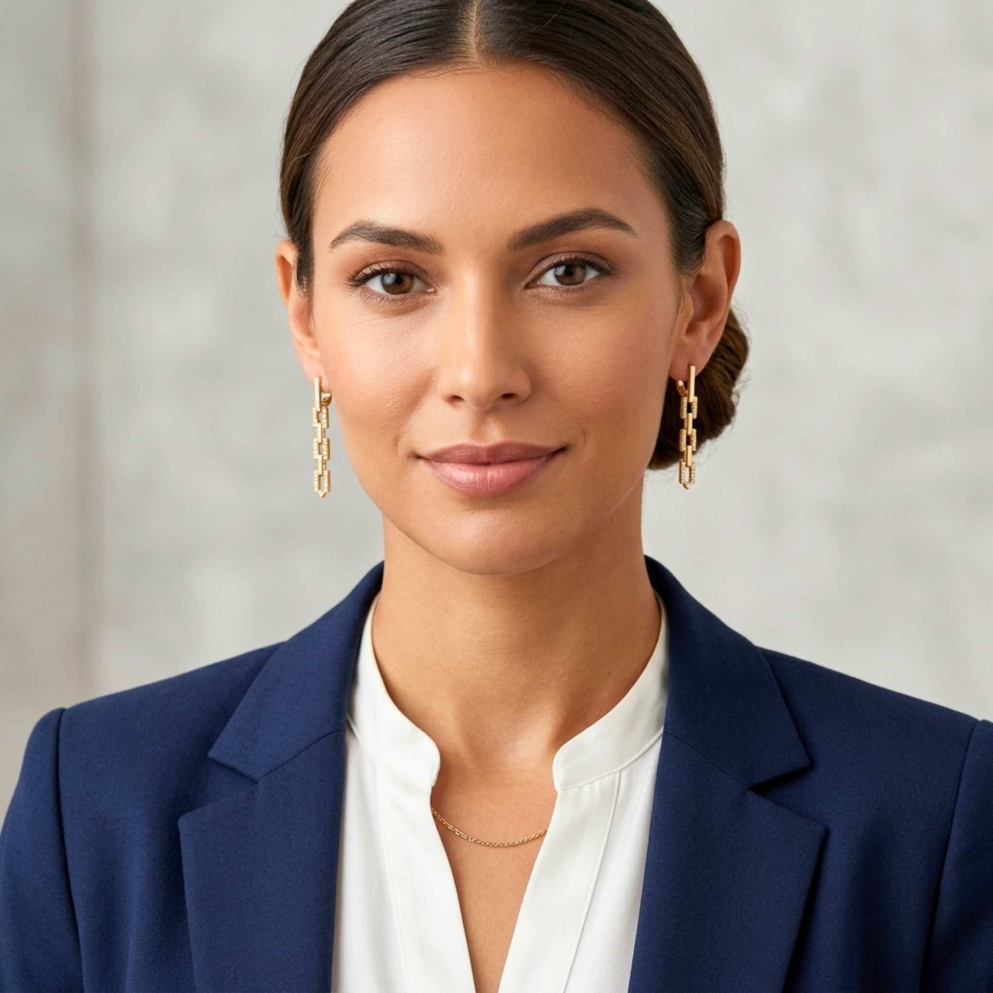 Woman wearing gold link earrings and blue blazer and white shirt against a neutral background.  Digitally rendered model for scale