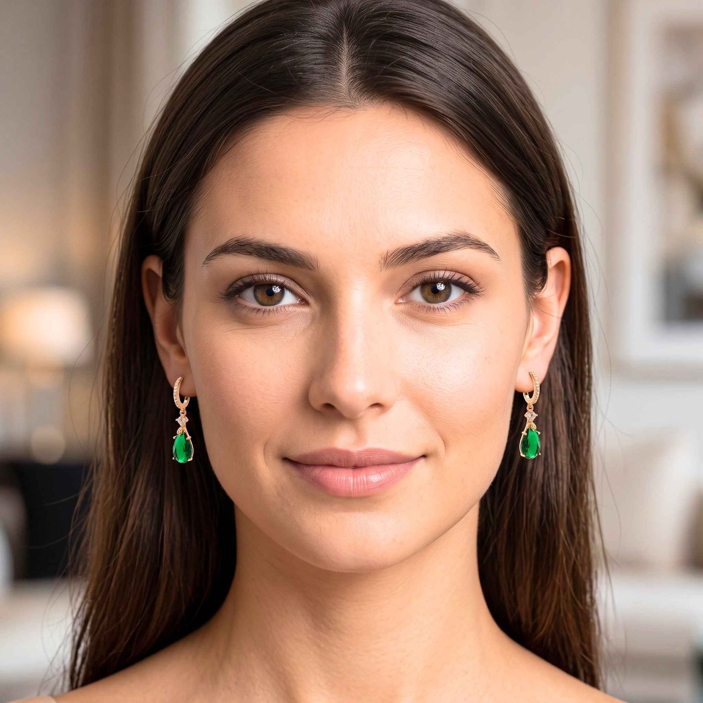 A close-up portrait of a woman wearing gold dangle earrings with green teardrop-shaped gemstones, set against a softly blurred indoor background.  Digitally rendered model for scale