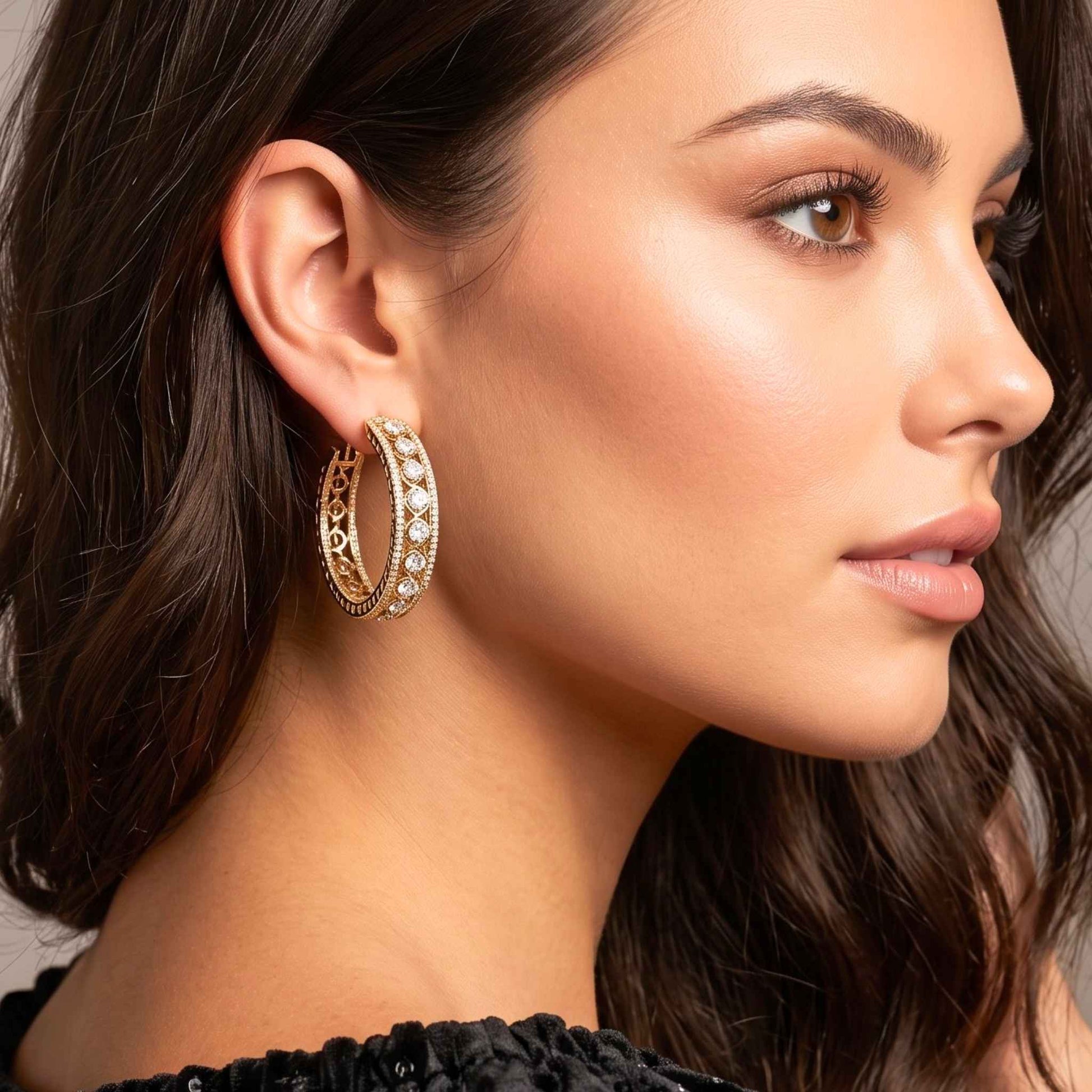 A close-up side profile of a woman wearing a pair of large gold hoop earrings adorned with clear pavé-style stones and openwork detailing.  Digitally rendered model for scale