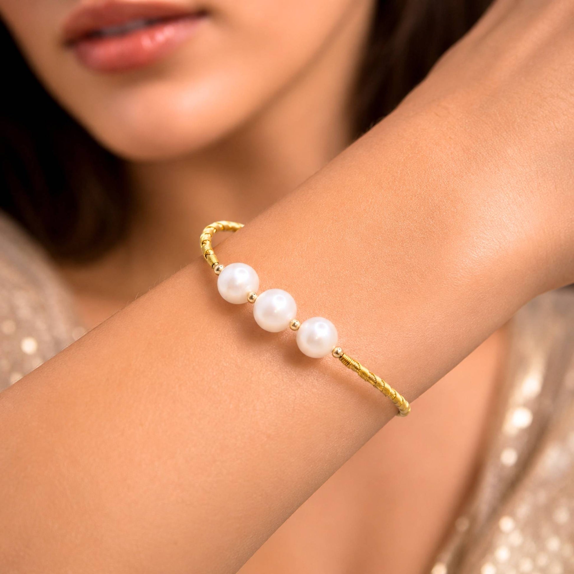 A close-up of a woman's wrist wearing a delicate gold cuff bracelet adorned with five white pearls.  Digitally rendered model for scale.
