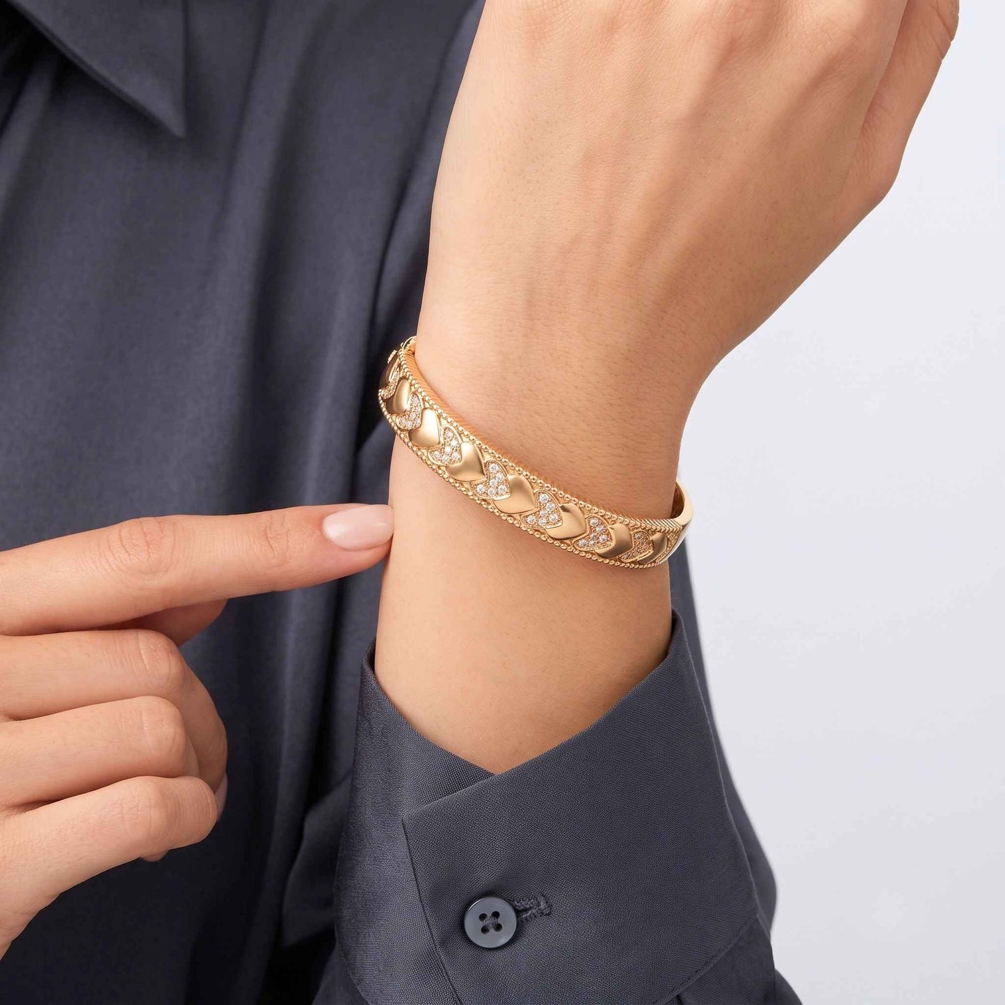 Gold heart bangle bracelet with alternating polished and cubic zirconia hearts, beaded edging and a concealed box clasp, shown worn on a person's wrist.  Digitally rendered model for scale