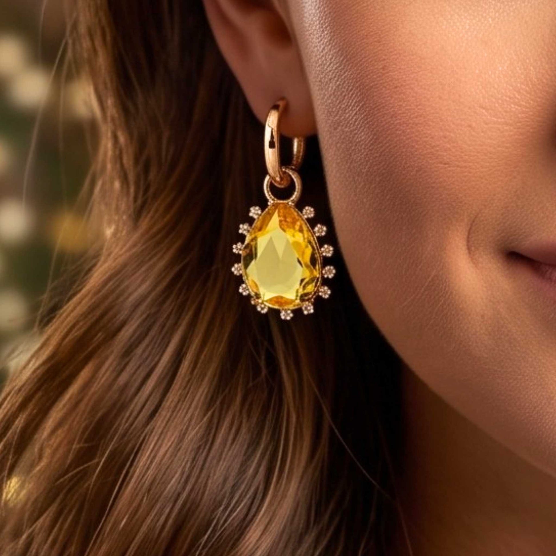 Close up of a woman with long brown hair wearing Gold hinged hoop drop earrings featuring pear-cut yellow stone surrounded by a delicate cubic zirconia halo on a polished gold finish from the Jewellery 4 Elegance collection.  Digitally rendered model for scale