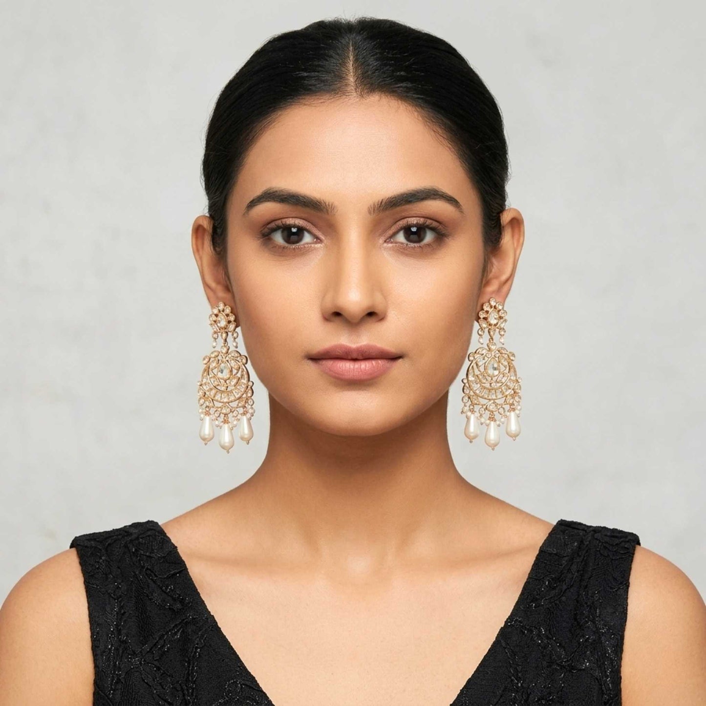 Woman wearing a black dress with gold Indian Chandbali chandelier drop earring featuring intricate cubic zirconia encrusting and dangling teardrop pearl beads from Jewellery 4 Elegance set against a neutral background.  Digitally rendered model for scale