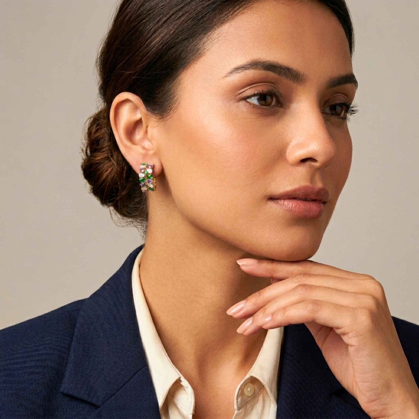 Woman wearing pair of quality gold hoop-style stud earrings adorned with an elegant mosaic of green, purple, pink gemstones set against a neutral background.  Digitally rendered model for scale.