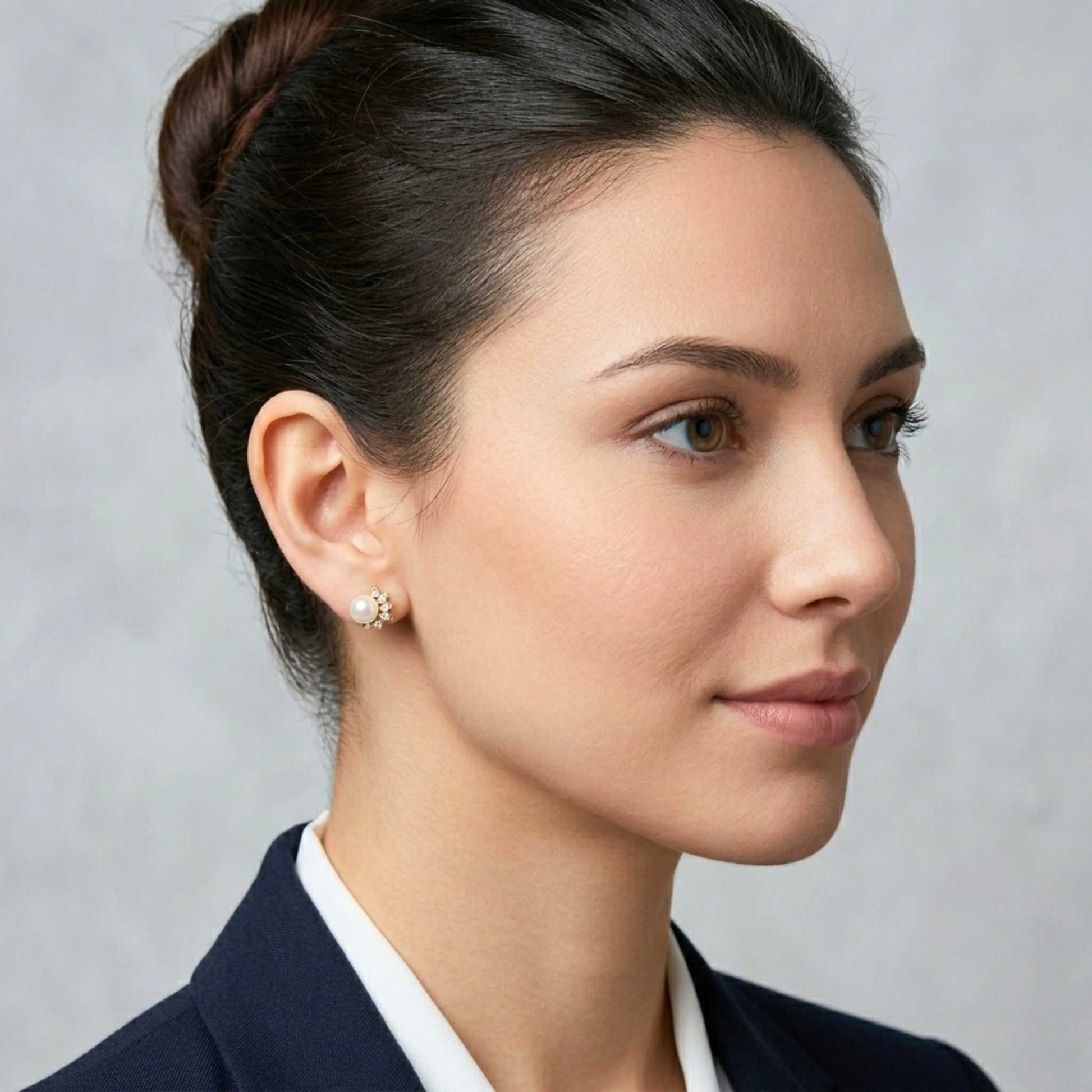 Woman wearing a dark blazer over a white shirt and pair of elegant gold stud earrings from Jewellery 4 Elegance featuring a lustrous central pearl accented by a sparkling curved cluster of round and marquise-cut cubic zirconia gemstones, set against a grey background.  Digitally rendered model for scale