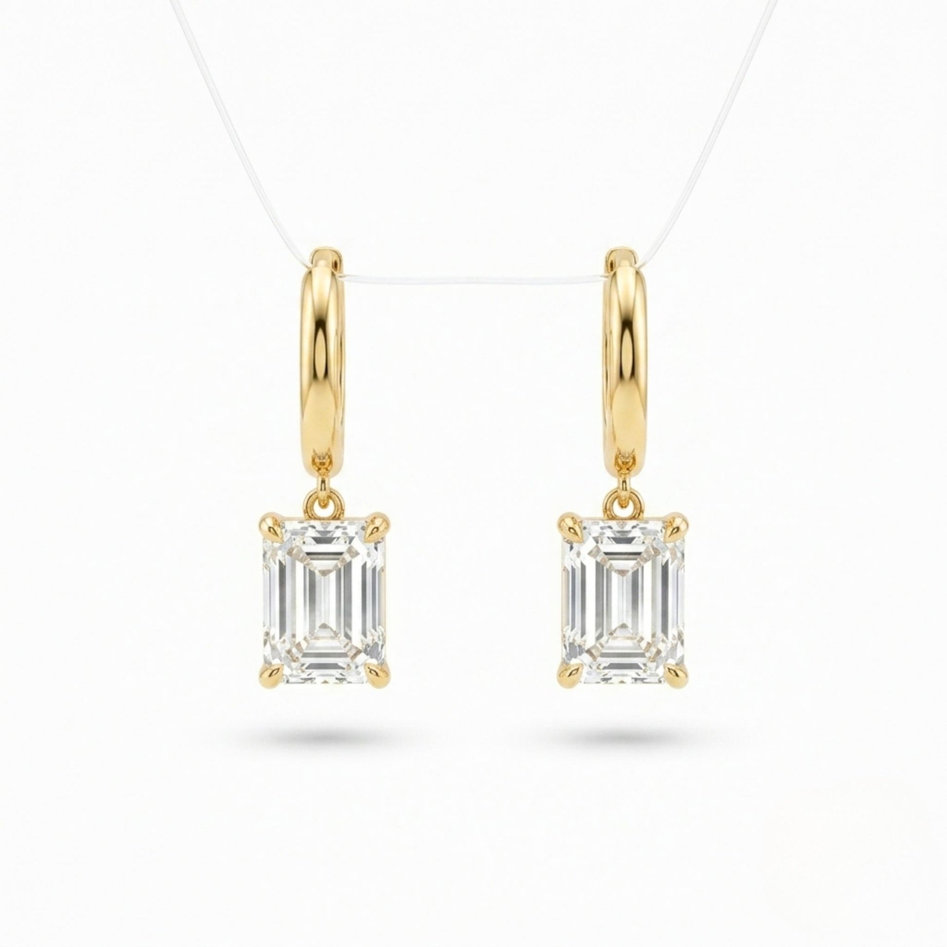 A pair of Jewellery 4 Elegance gold plated drop earrings featuring smooth huggie hoops suspending a brilliant emerald cut cubic zirconia gemstone on a white background