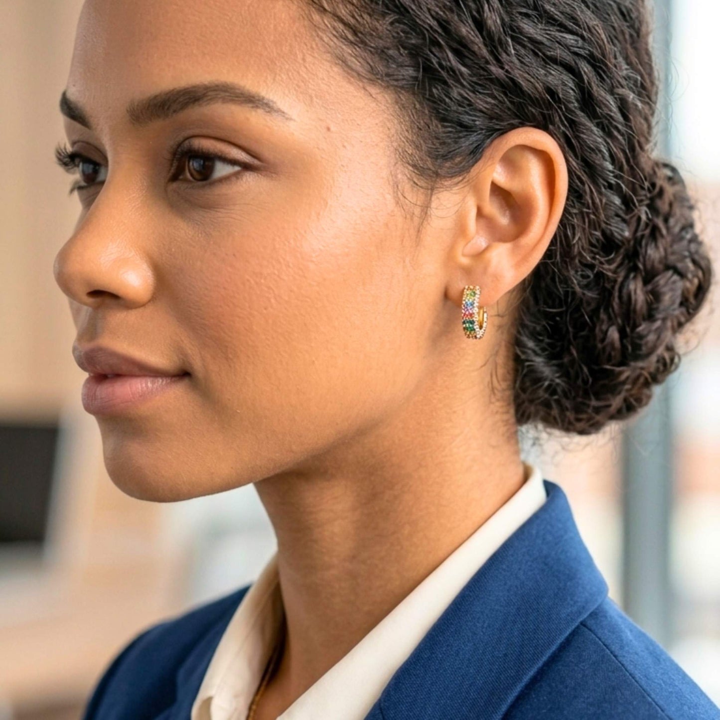 Close-up of a woman wearing Gold plated hoop earrings featuring rows of multicoloured pavé-set cubic zirconia stones in an elegant rainbow design.  Digitally rendered model for scale