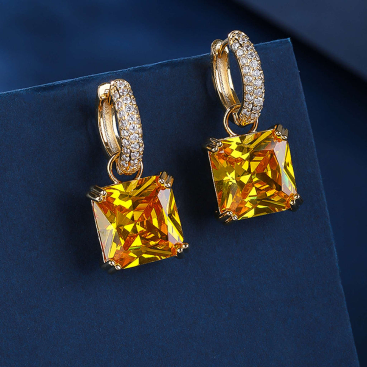 Gold hoop earrings with large yellow gemstones from the Jewellery 4 Elegance collections on a dark blue background