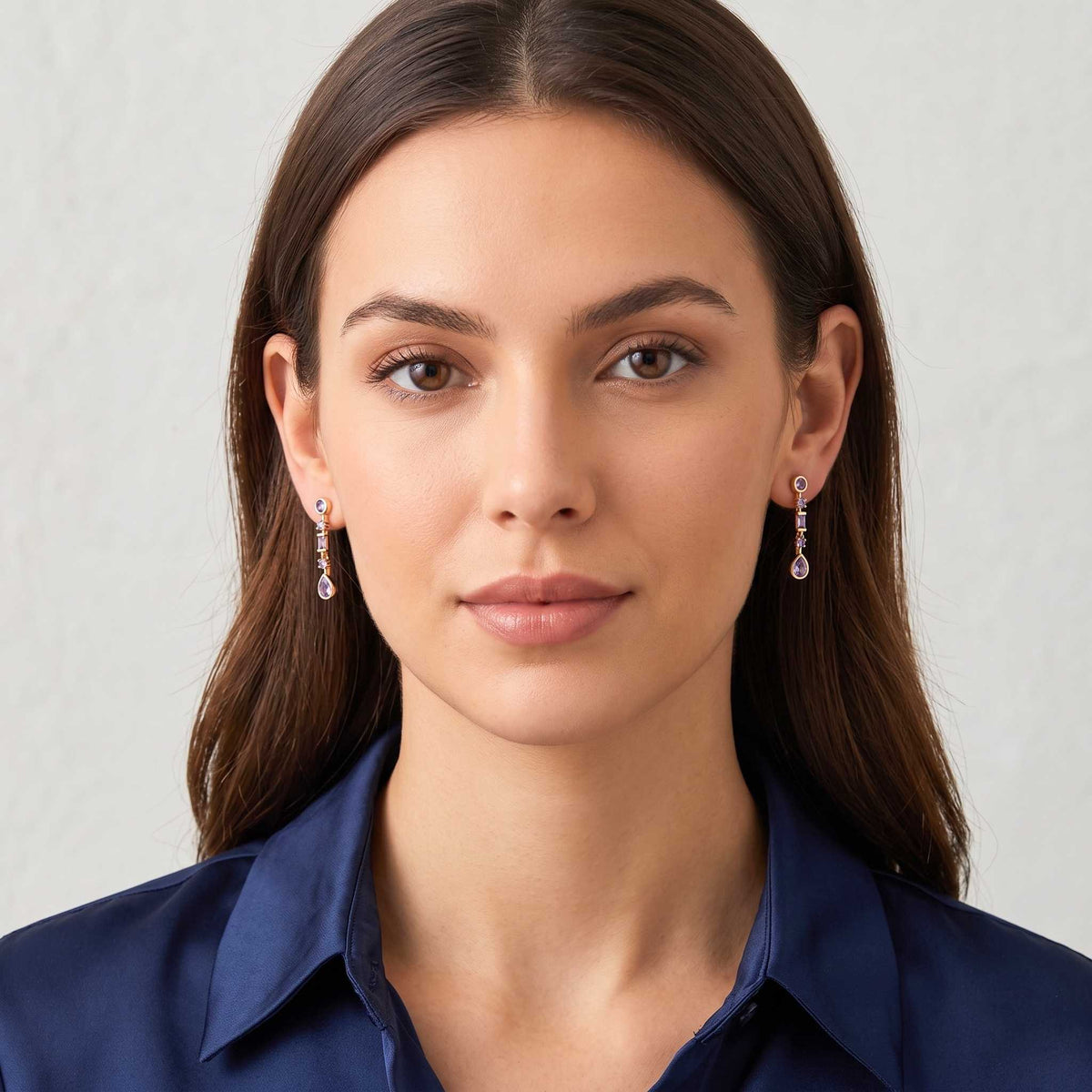 A close-up portrait of a woman wearing  purple gemstone drop earrings with teardrop-shaped drops, paired with a navy blue collared shirt against a light grey background.  Digitally rendered model for scale