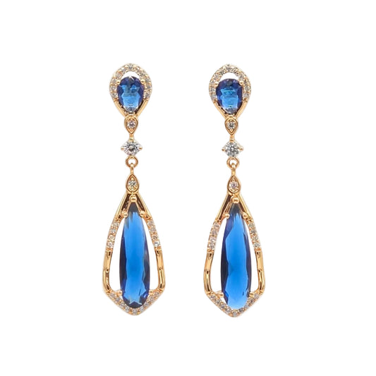 A pair of gold drop earrings featuring oval blue gemstones at the top and larger teardrop-shaped blue gemstones hanging below, accented with small clear stones, shown on a plain white background from the Jewellery 4 Elegance collection.