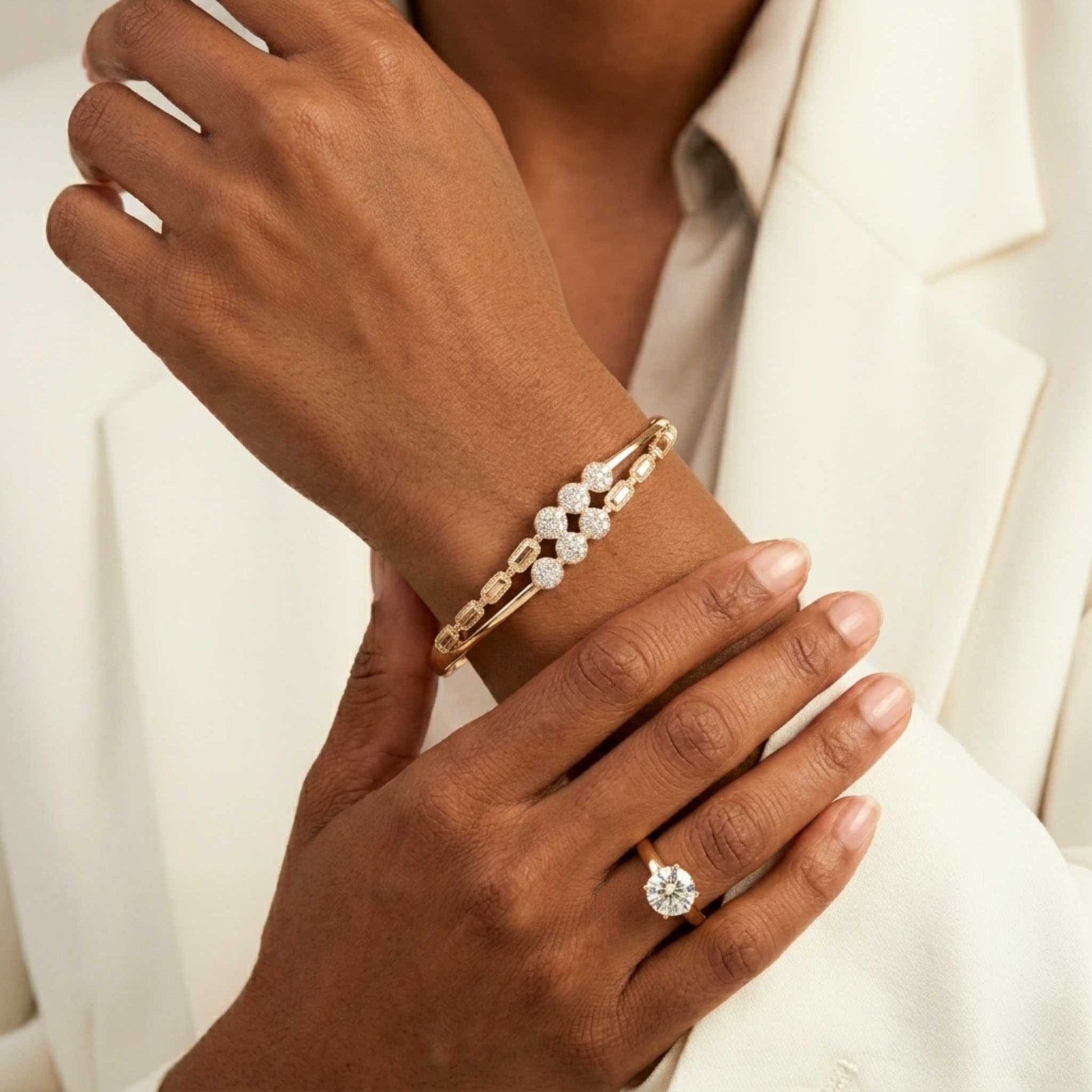 Close-up of a hand wearing a gold bangle bracelet and diamond ring on a white background